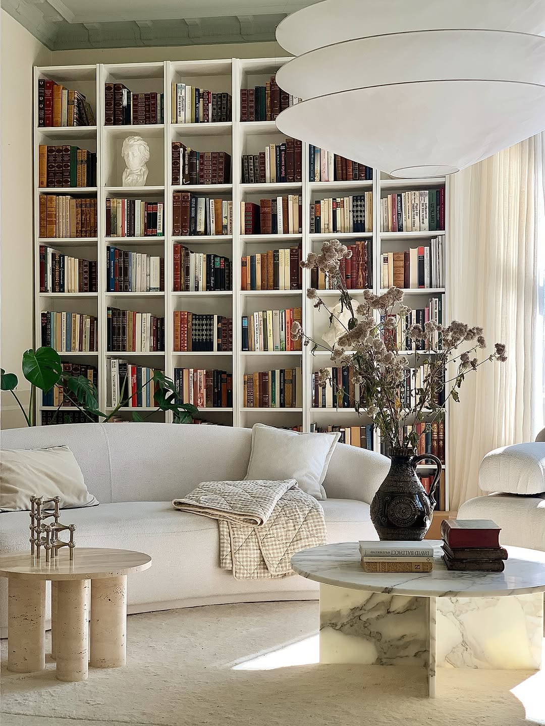 Helles Wohnzimmer mit großer Bücherwand, Sofa und Vase mit Trockenblumen von blomus auf dem Couchtisch