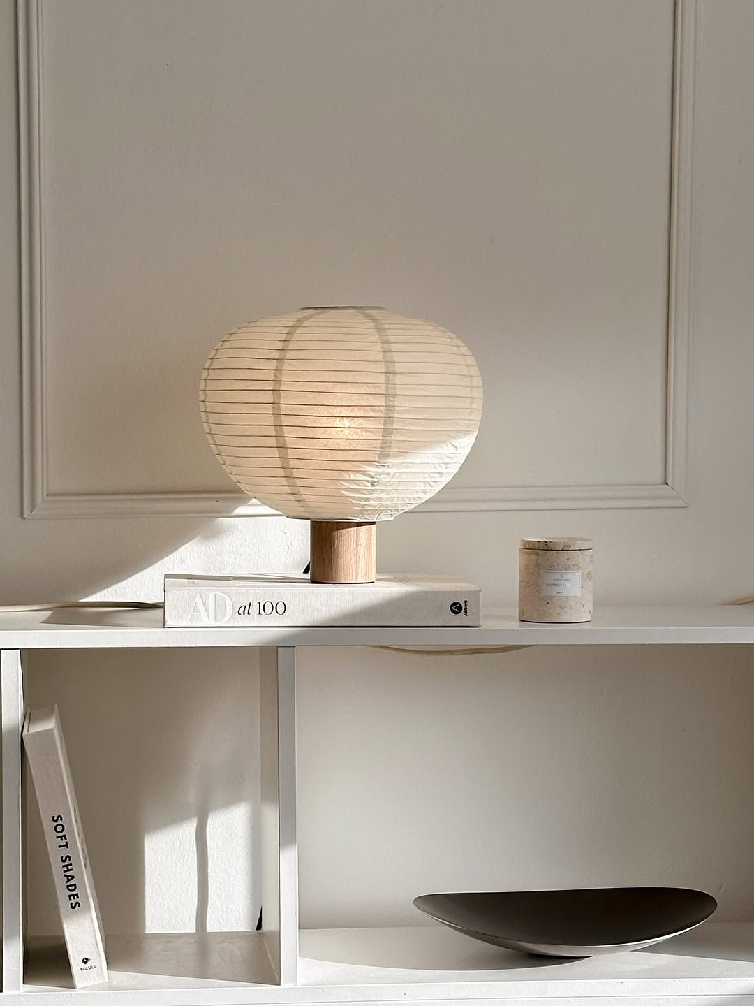 Minimalistisches Regal mit Tischlampe, Büchern und blomus Duftkerze in hellem Wohnraum