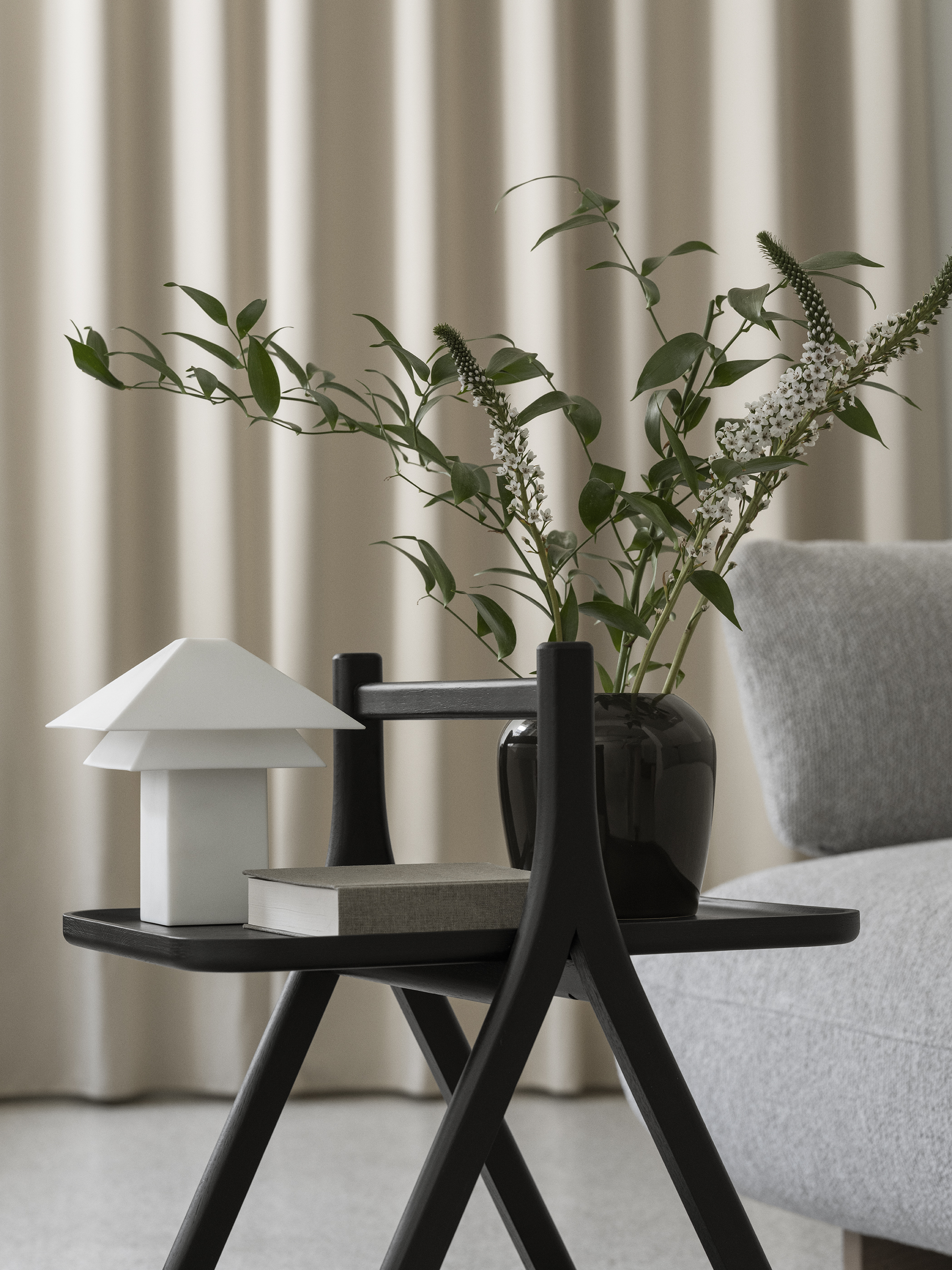 Eleganter Beistelltisch mit blomus Vase und Zweigen neben Sessel in modernem Wohnzimmer