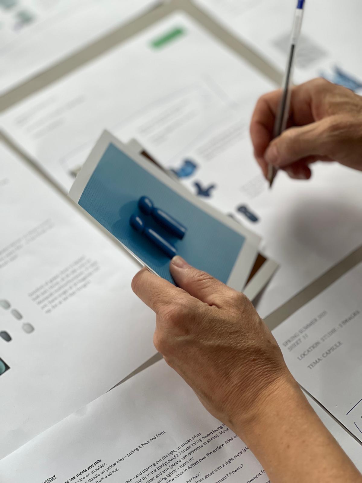 Nahaufnahme von Händen, die Produktausdrucke und Farbmuster prüfen und während eines kreativen Designprozesses Notizen machen.