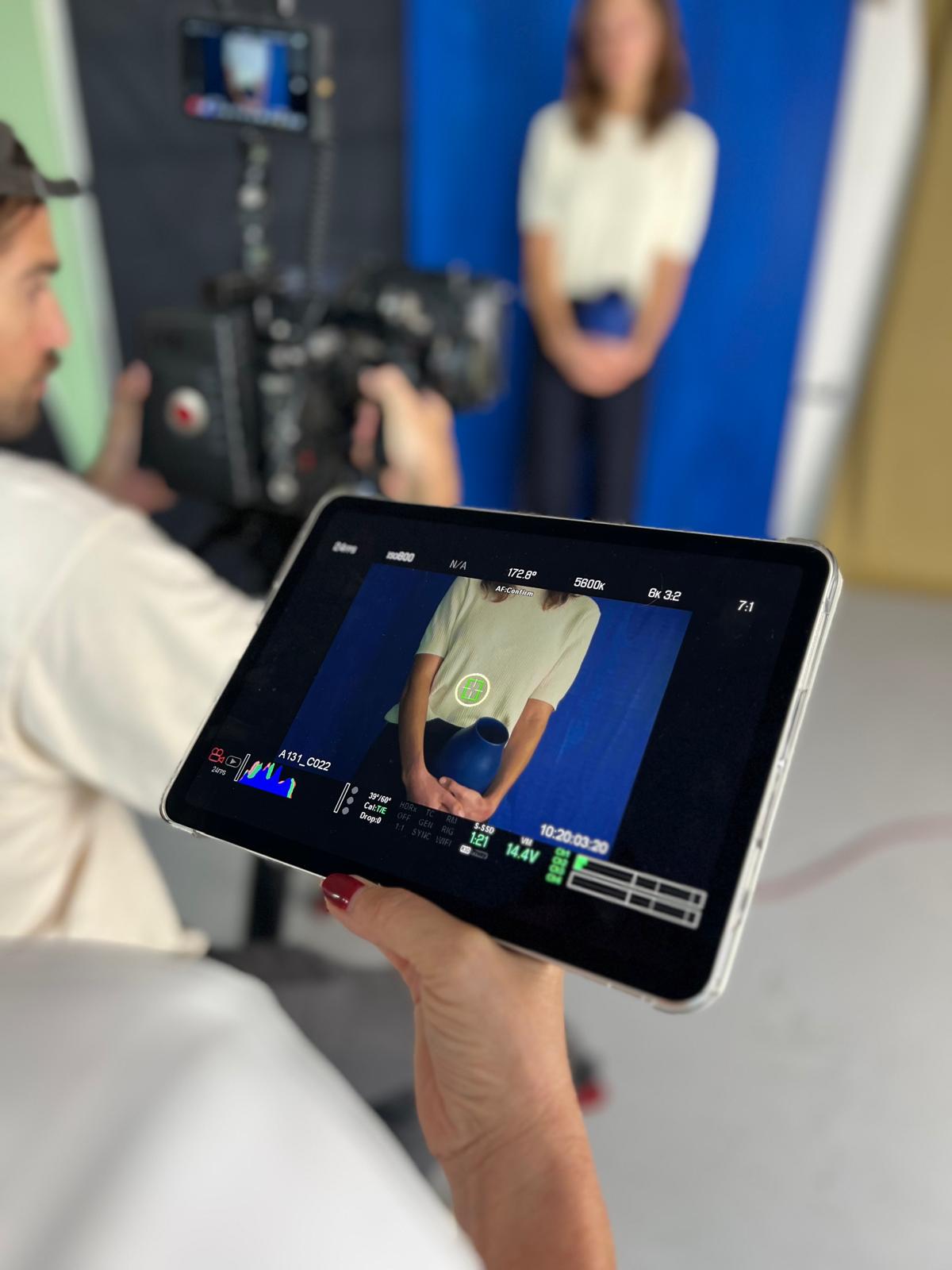 Behind-the-Scenes-Produktfotoshooting mit Kamerateam, das ein Model mit blauer Vase filmt, kontrolliert über ein Tablet.