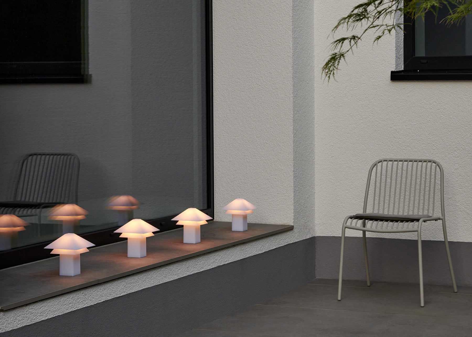 Modern outdoor setting with glowing mushroom lamps and a minimalist chair by the window.